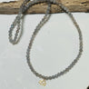 Beaded necklace with a gold cancer charm on a white surface