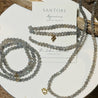 Gray beaded bracelets with gold zodiac charm accents on a white plate, featuring Santore branding.
